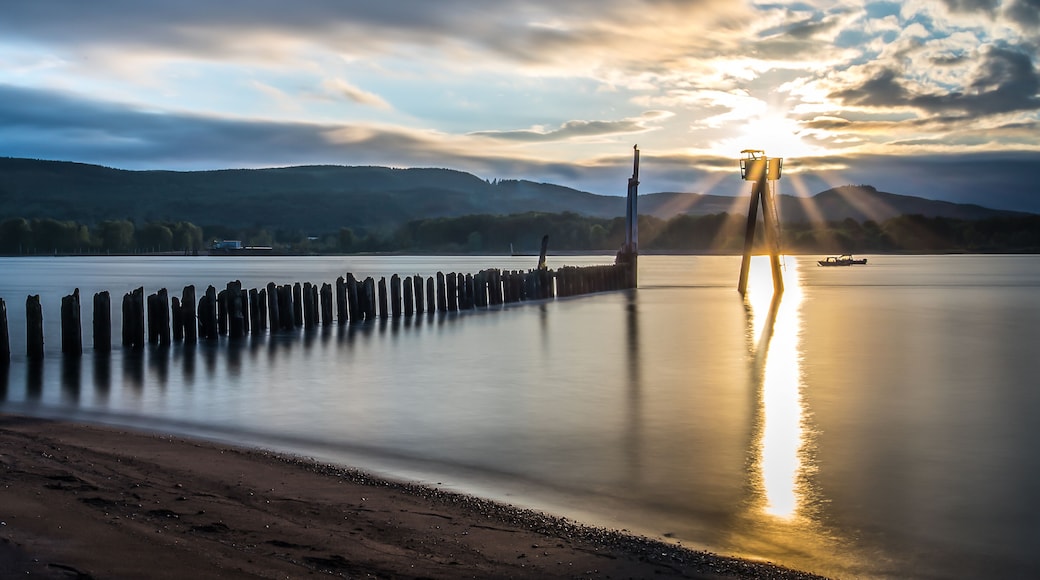 A calm lake with a wooden pier, a lighthouse, and a sunset.
