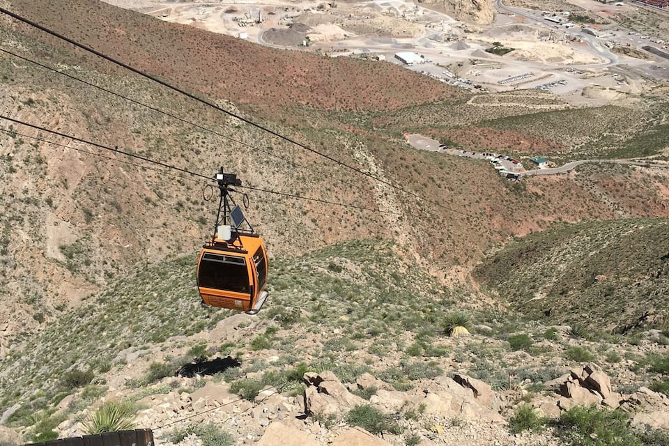 A cable car in a desert landscape with distant urban areas.