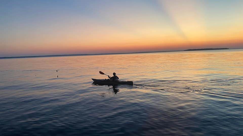 A kayaker on a calm body of water during sunset.