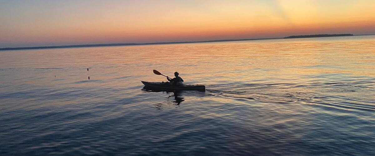A kayaker on a calm body of water during sunset.