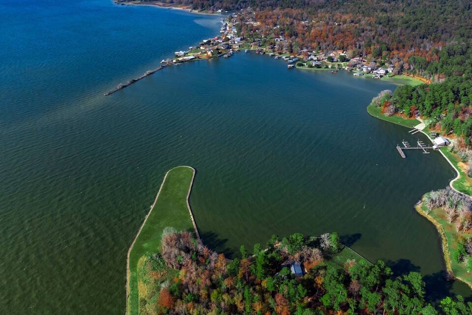 An aerial view of a lake with a dock, surrounded by dense forest and residential areas.