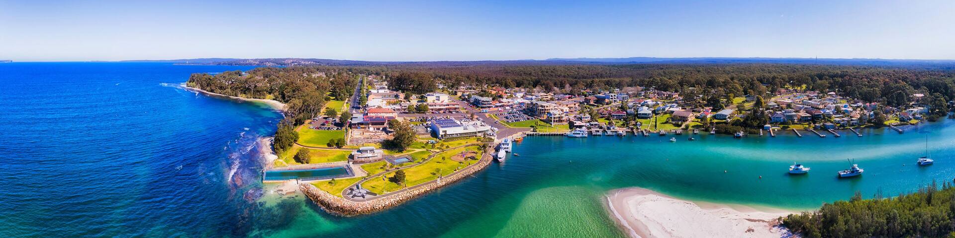 An aerial view of a coastal town with a marina, clear turquoise waters, and a sandy beach.