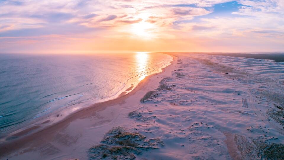 A coastal landscape with a beach, ocean, and a sunset.