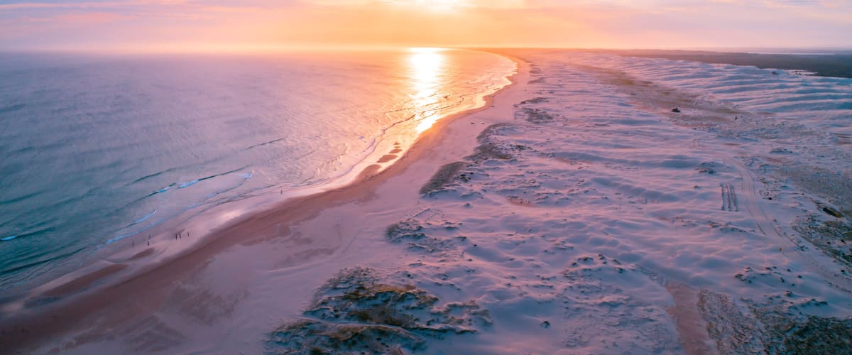 A coastal landscape with a beach, ocean, and a sunset.