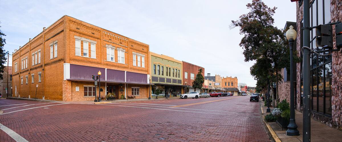 A historic street lined with brick buildings, a cobblestone road, and a stone building with a clock tower.