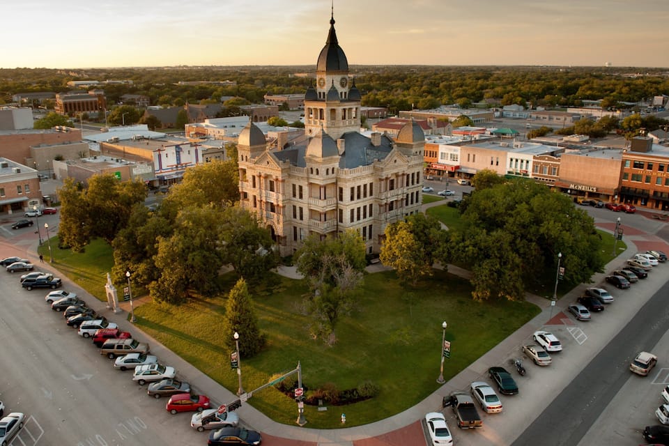 A large historic building with a clock tower surrounded by a parking lot and trees.