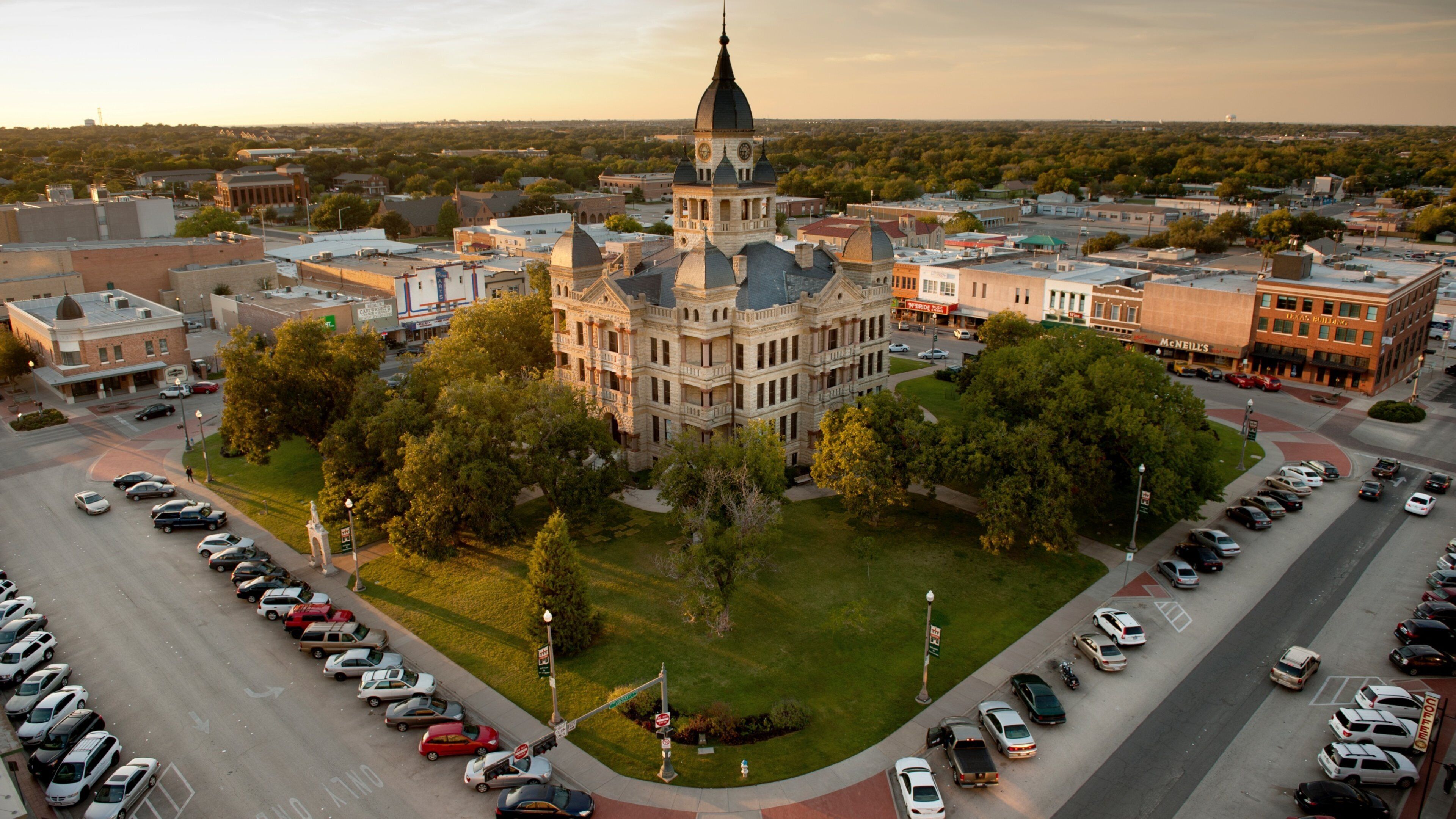 A large historic building with a clock tower surrounded by a parking lot and trees.