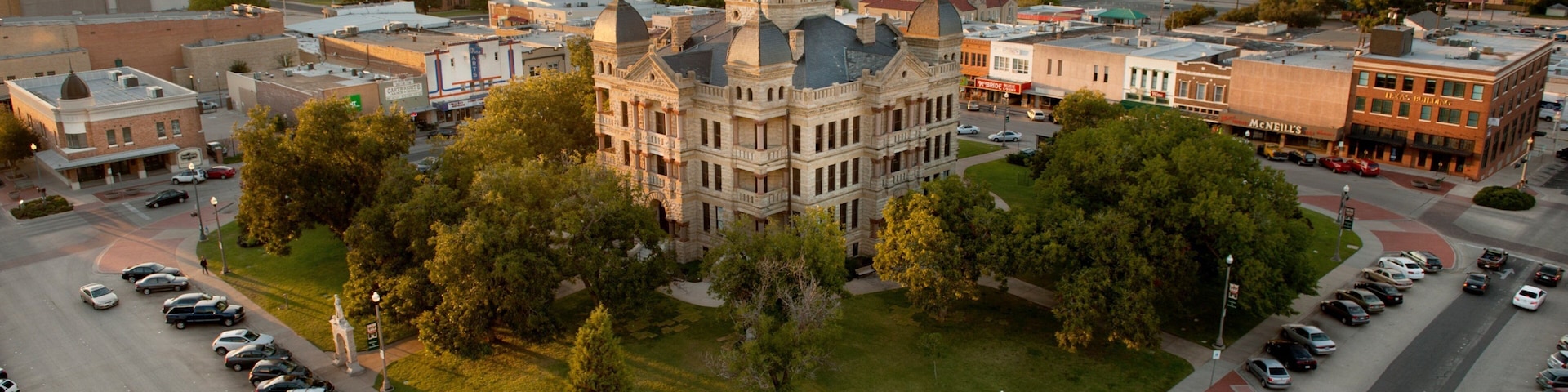 A large historic building with a clock tower surrounded by a parking lot and trees.