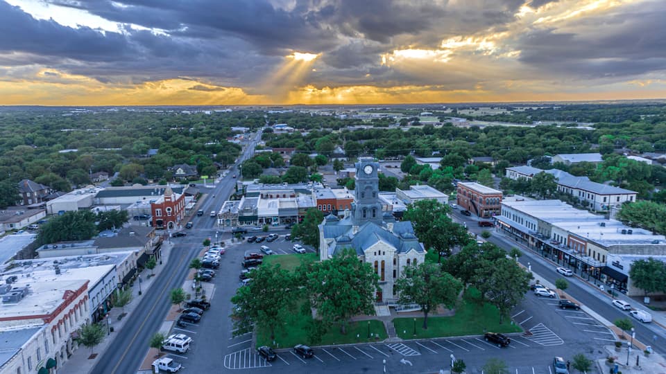 A town square with a prominent clock tower, surrounded by historic buildings and a large parking lot.