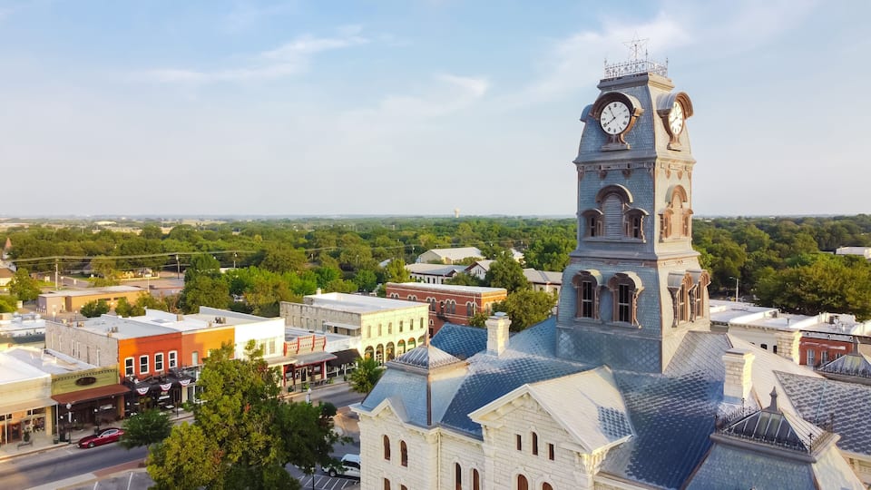 A historic town with a prominent clock tower, surrounded by lush greenery and traditional architecture.