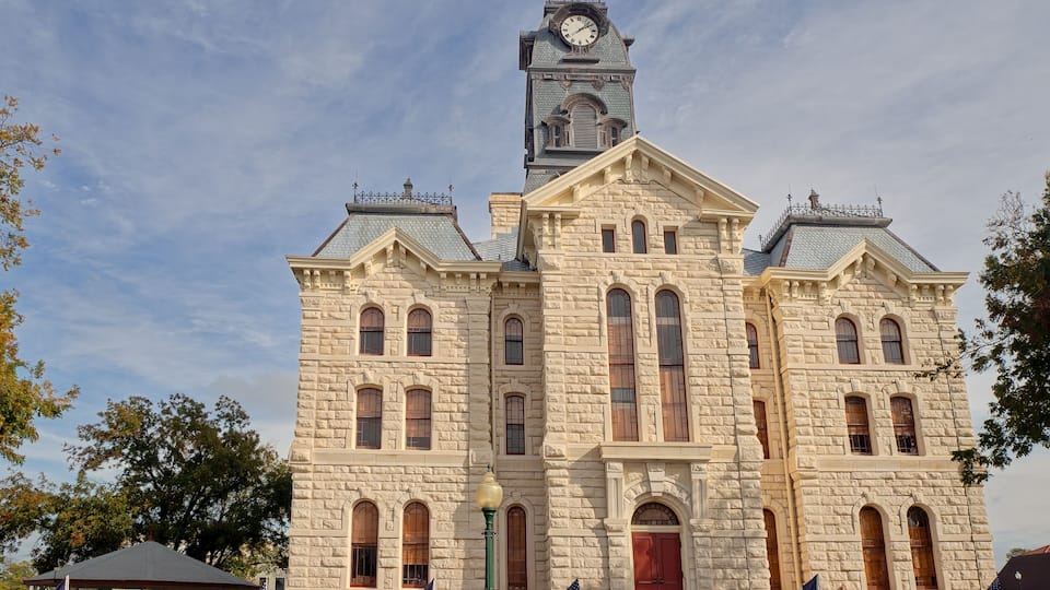 A historic stone building with a clock tower, multiple arched windows, and flags.