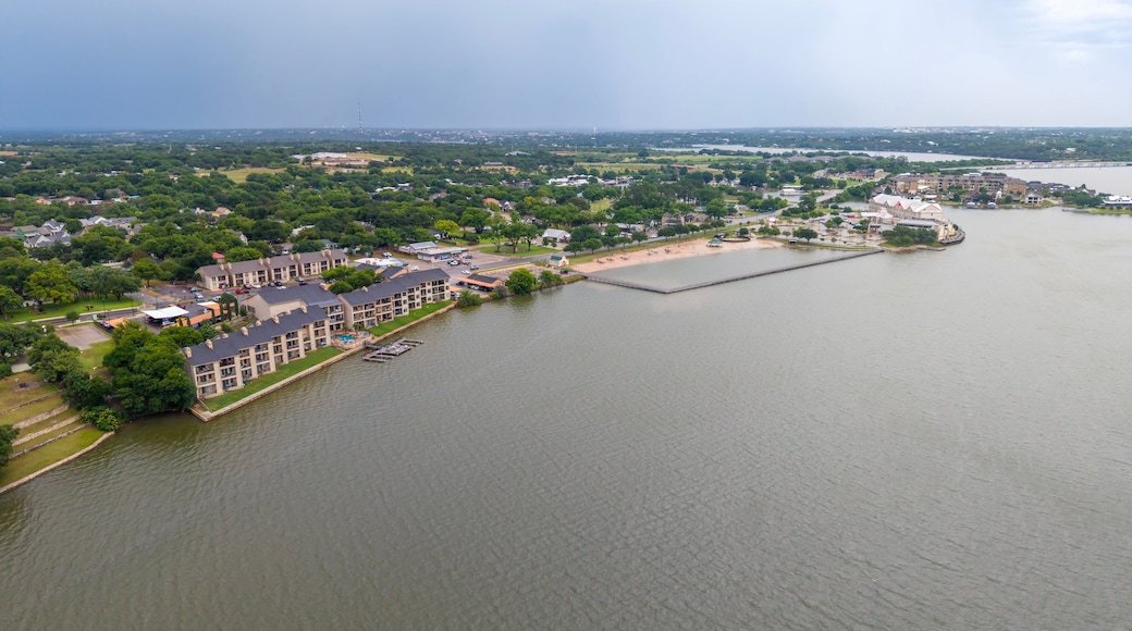An aerial view of a riverside residential area with a dock, a bridge in the distance, and a large body of water.
