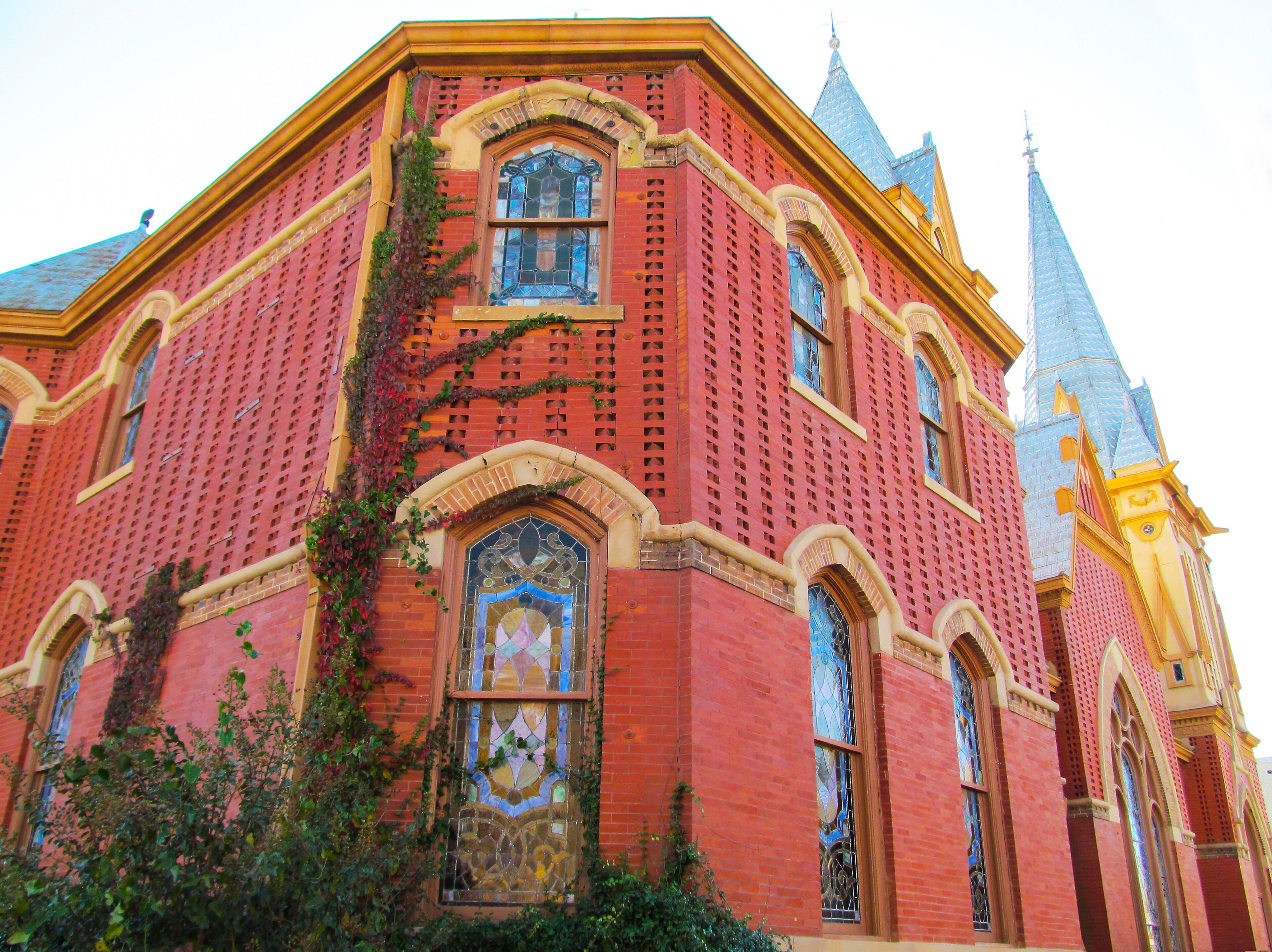 Beautiful church building in Greenville, TX, USA. Bright red brick wall of house with stained-glass windows and decor detail against blue sky.