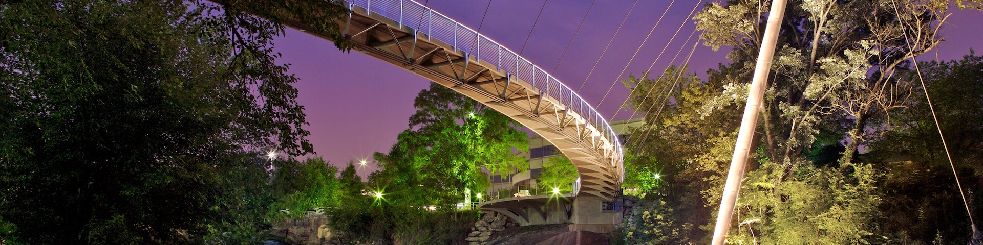 Un puente colgante nocturno sobre un río, rodeado de árboles y rocas.
