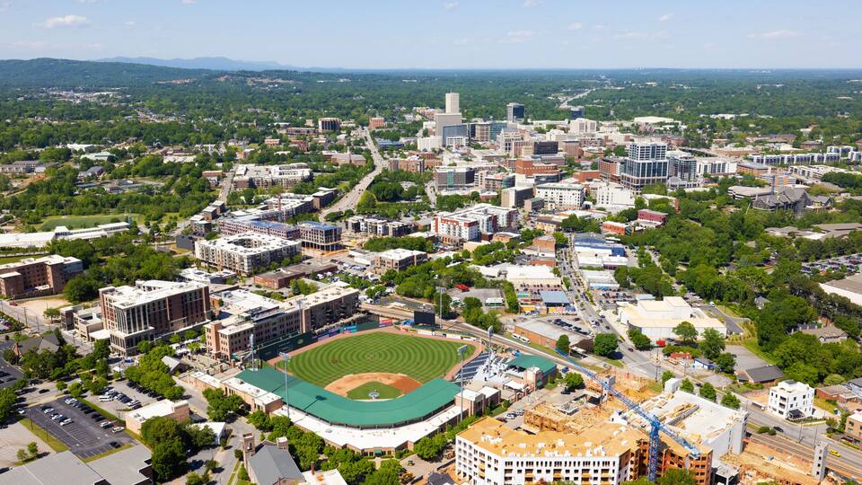 A cityscape with a baseball stadium, surrounding buildings, and a distant mountain range.