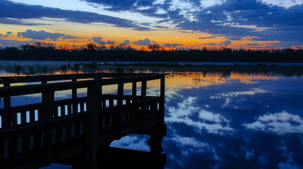 A sunset over a calm lake with a wooden bridge reflecting the sky.
