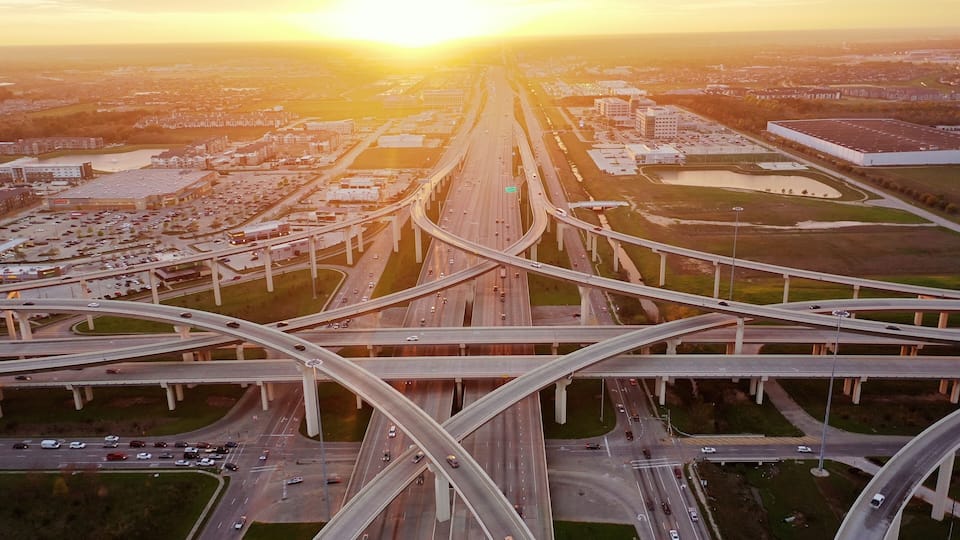 An aerial view of a complex highway interchange with multiple overpasses and a large parking lot.