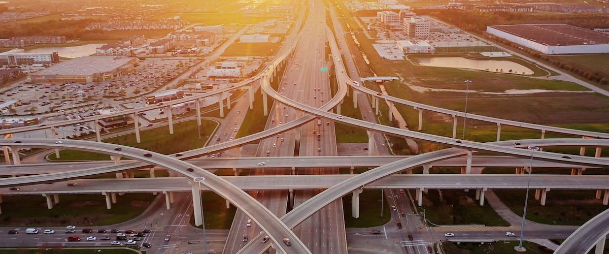 An aerial view of a complex highway interchange with multiple overpasses and a large parking lot.