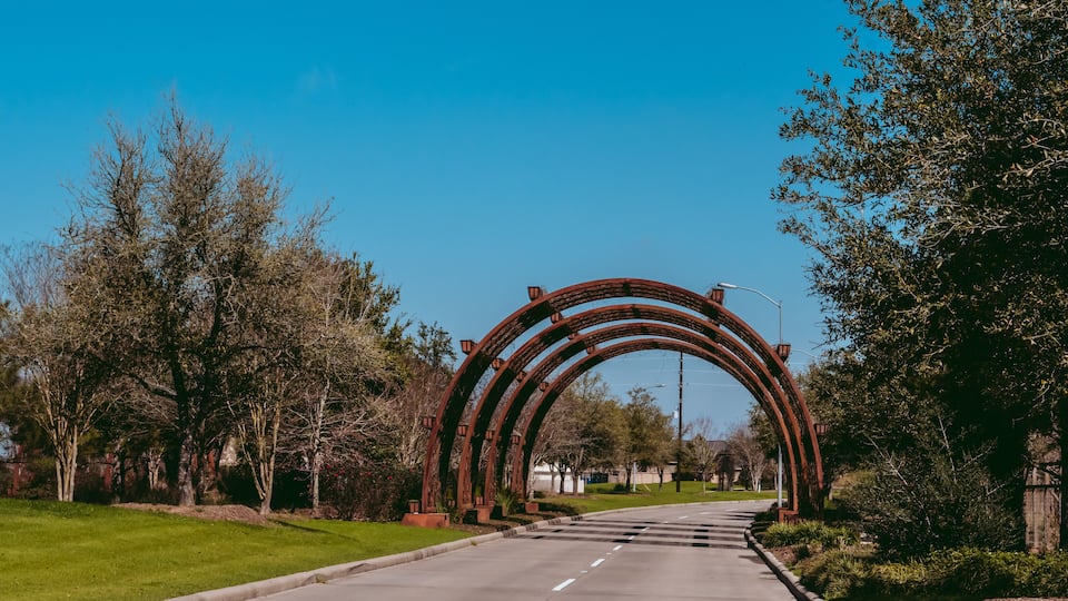 A road passing under a large metal archway with trees on either side.
