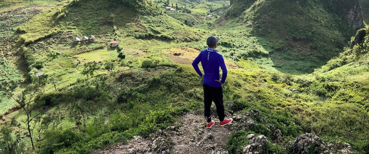 A hiker overlooking a lush valley with green hills and scattered houses.