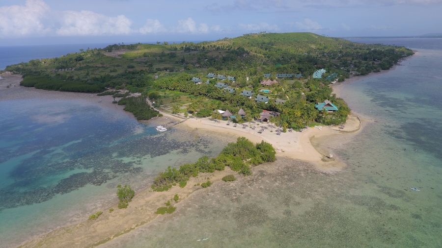 Una isla con playa, aguas cristalinas y varios edificios con techos verdes.