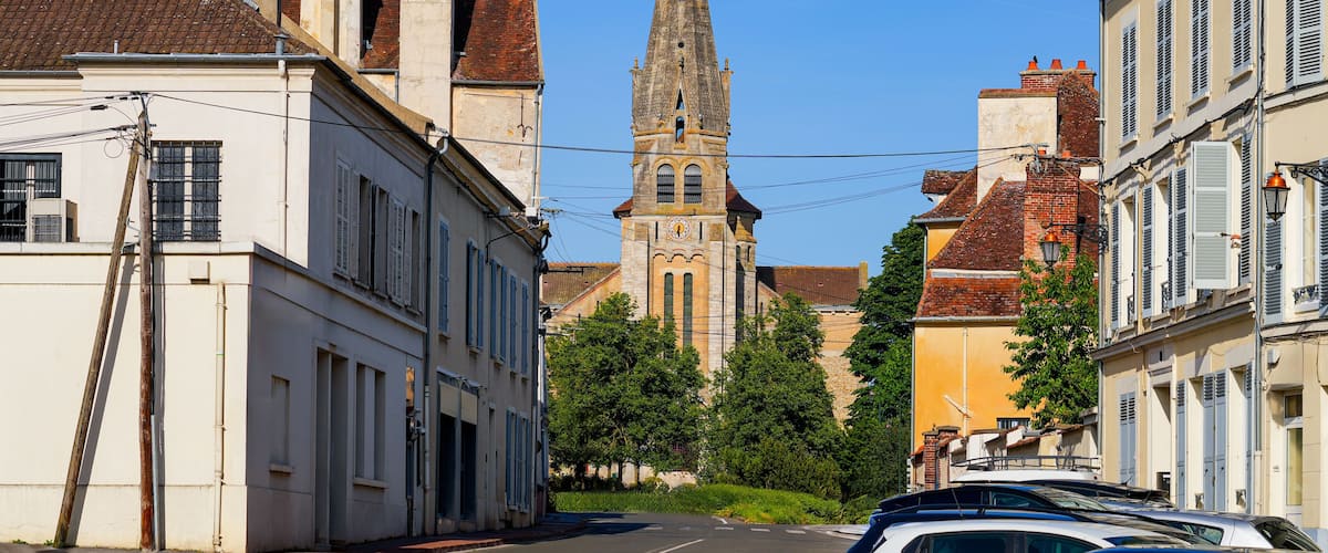 A street with historic buildings, a church tower, and parked cars.