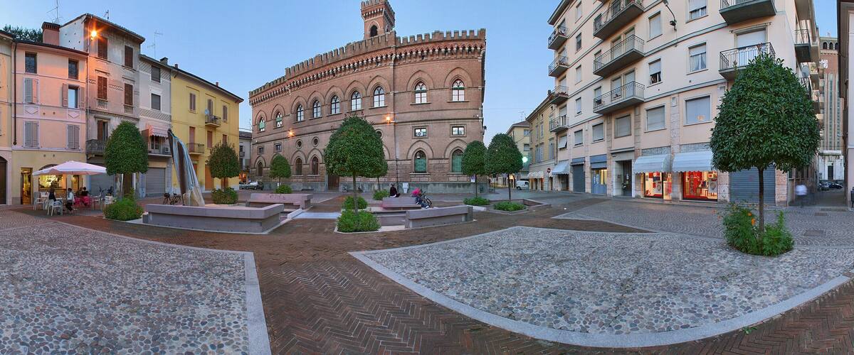 A cobblestone square with historic buildings, a fountain, and trees.