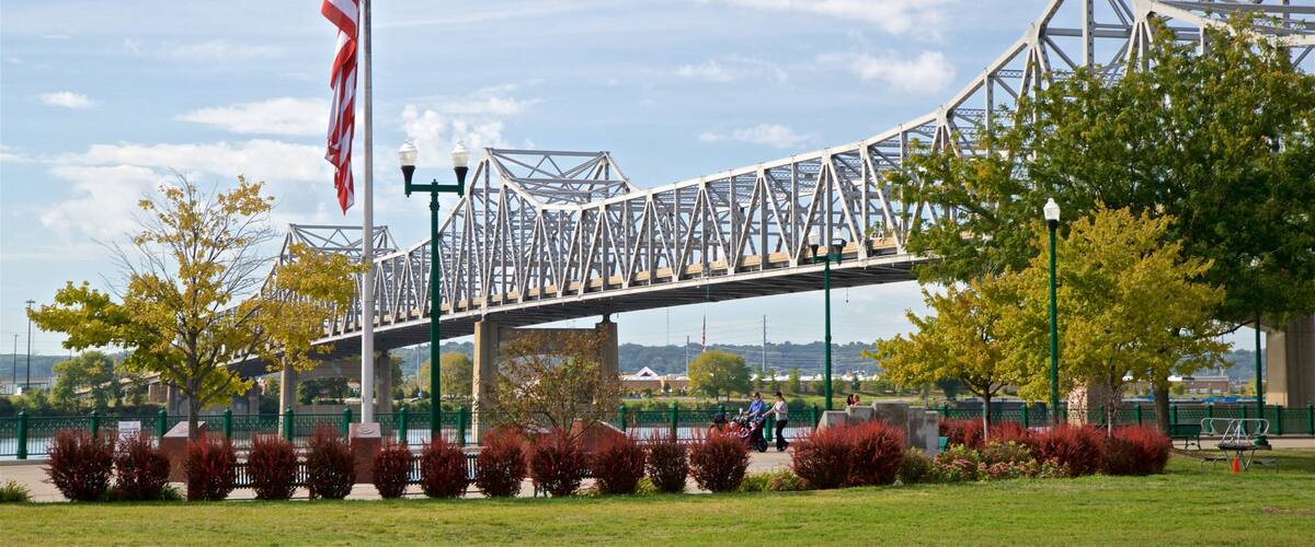 A steel bridge with an American flag, surrounded by green trees and grass.