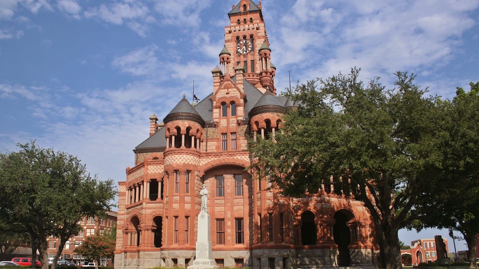 A historic building with a clock tower, arched windows, and a statue in front.
