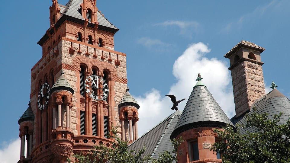 A historic building with a prominent clock tower, intricate architectural details, and a bird flying near the roof.