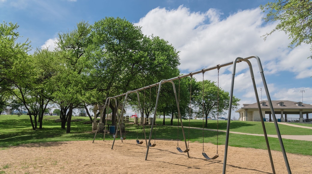Close-up swing set 6 seats in nature park and tree lush at Ennis, Texas, USA. Outdoor sand playground hanging seat suspended from bar swings back and forth surround by leaves green, cloud blue sky
