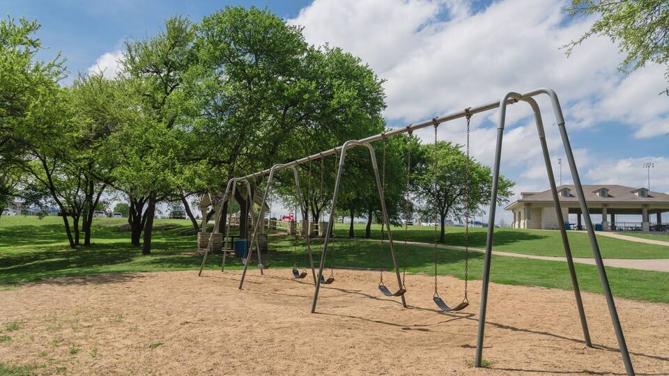 A park with a swing set, green trees, and a building in the background.