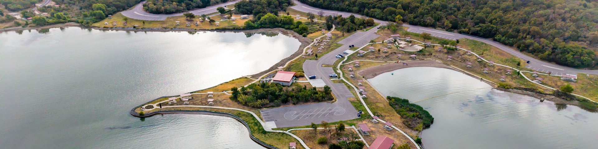 An aerial view of a lake with a small island featuring a parking lot, buildings, and a road.