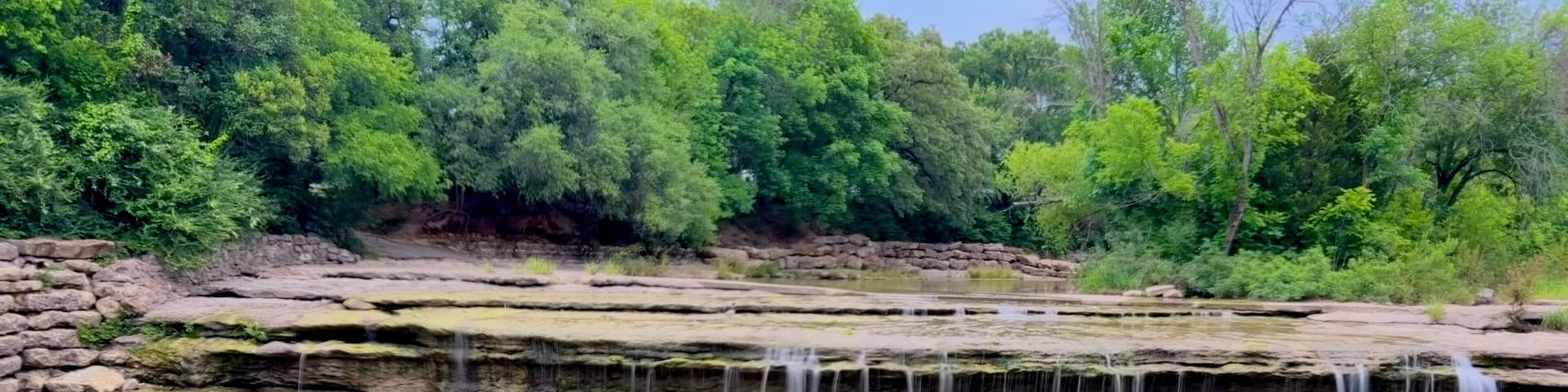 A multi-tiered waterfall cascading over rocky ledges surrounded by dense greenery.
