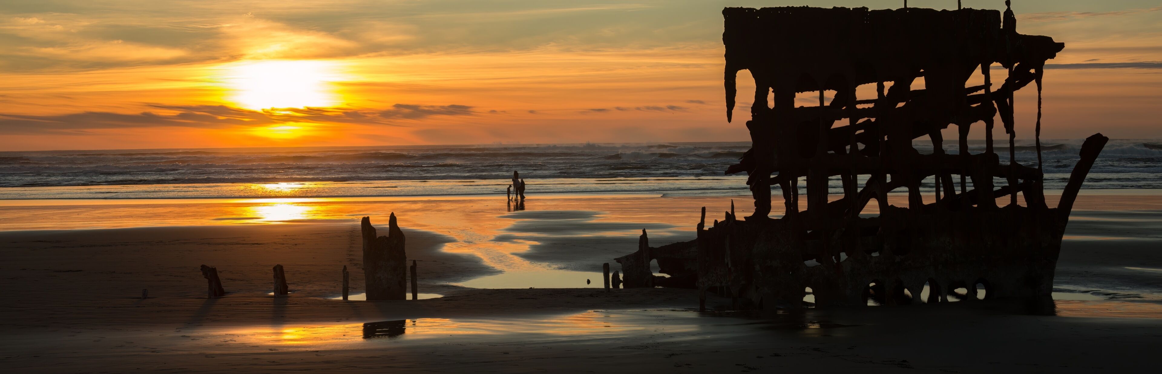 A sunset over a beach with a large, rusted shipwreck.
