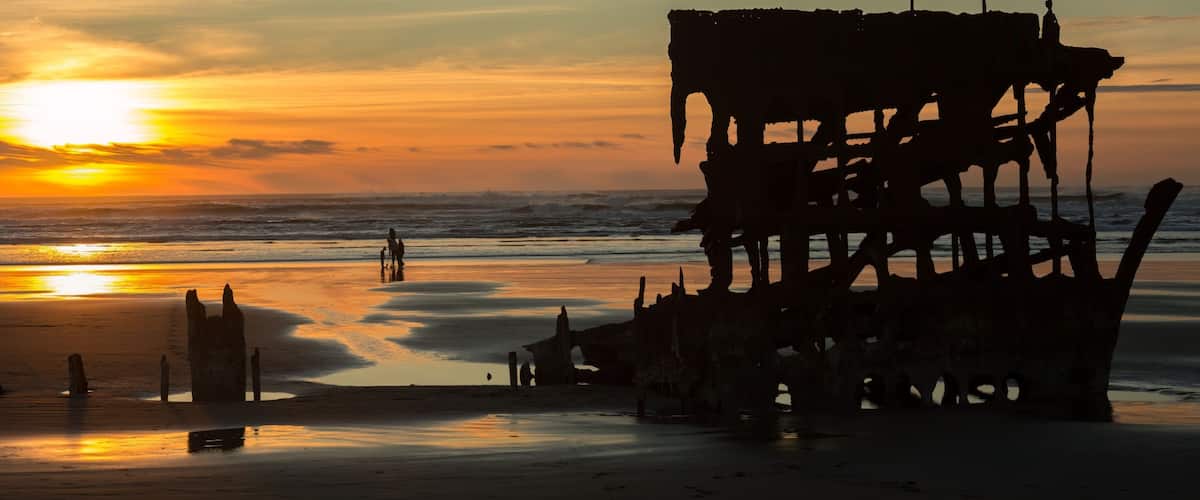 A sunset over a beach with a large, rusted shipwreck.