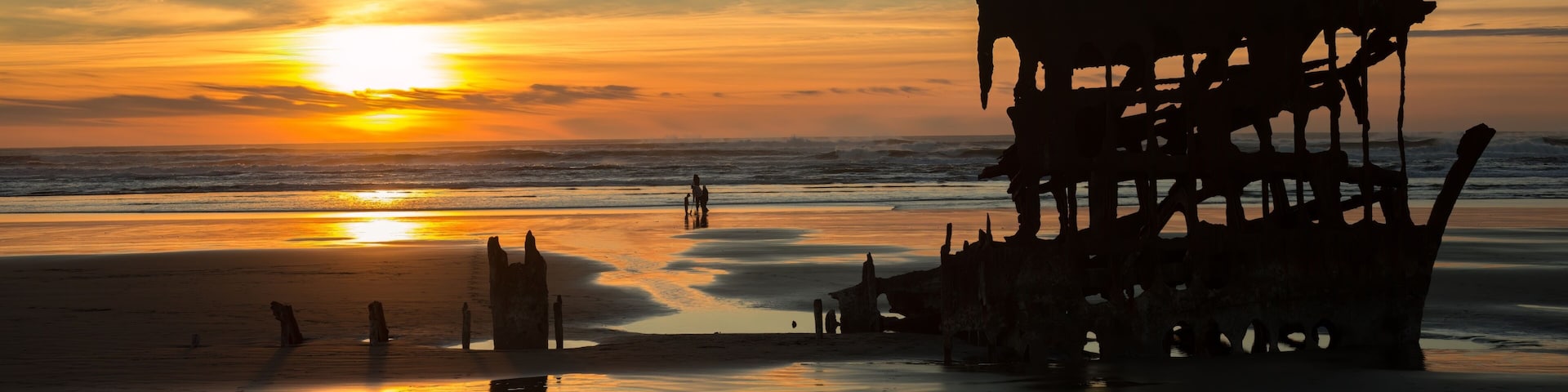 A sunset over a beach with a large, rusted shipwreck.