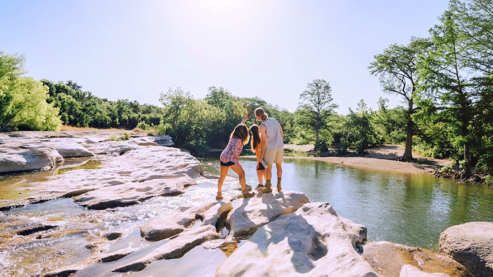 Friends posing for cell phone selfie on rocks near river