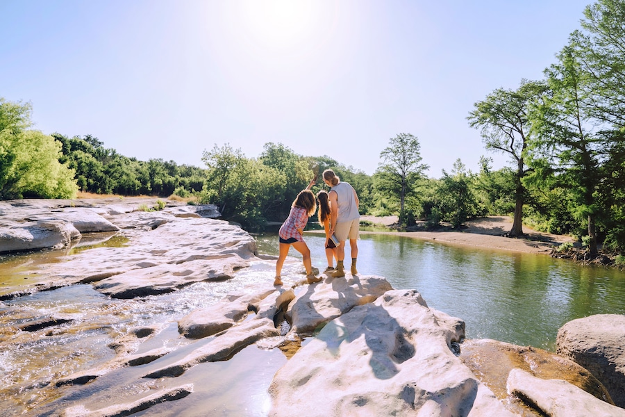 Friends posing for cell phone selfie on rocks near river