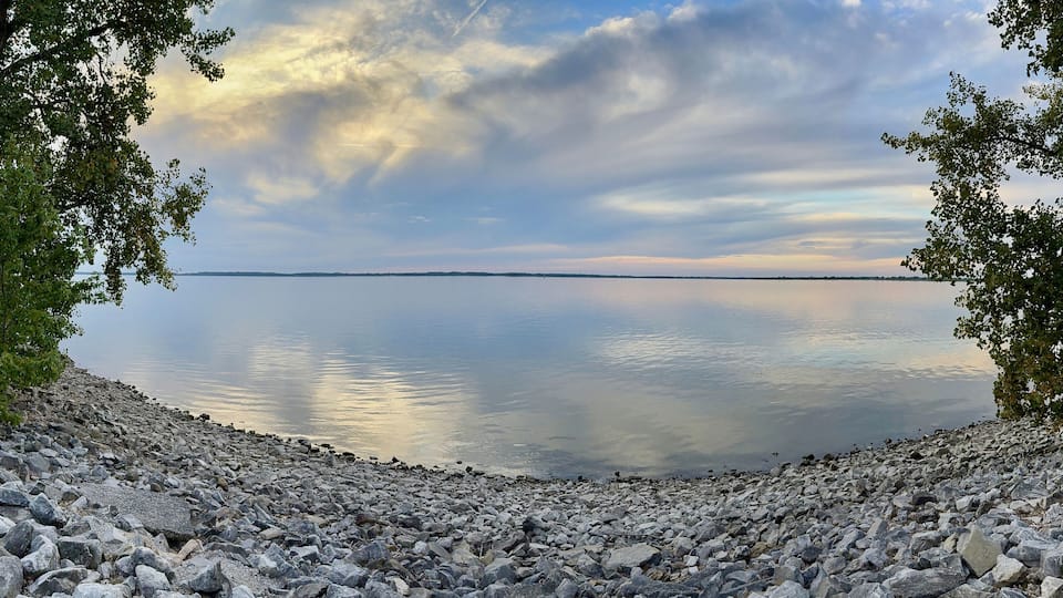 A rocky shoreline with calm water reflecting the sky.
