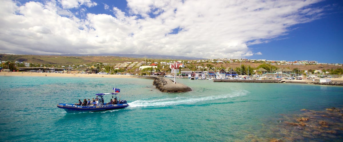 A boat on turquoise waters near a coastal town with buildings and a rocky outcrop.
