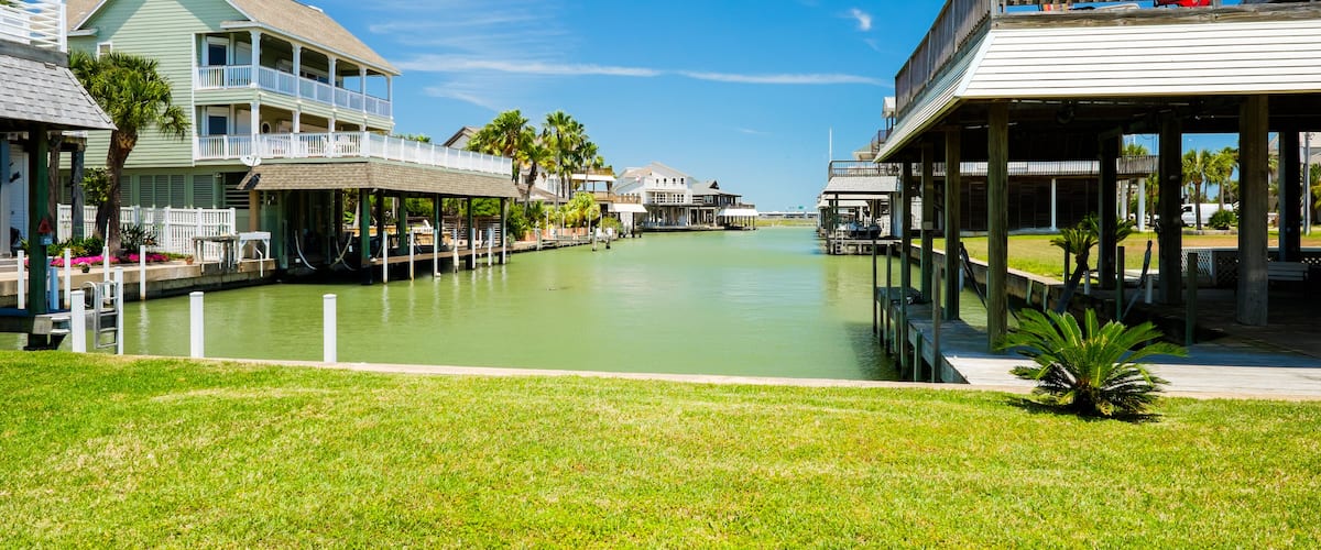 A canal with waterfront houses, palm trees, and a clear blue sky.