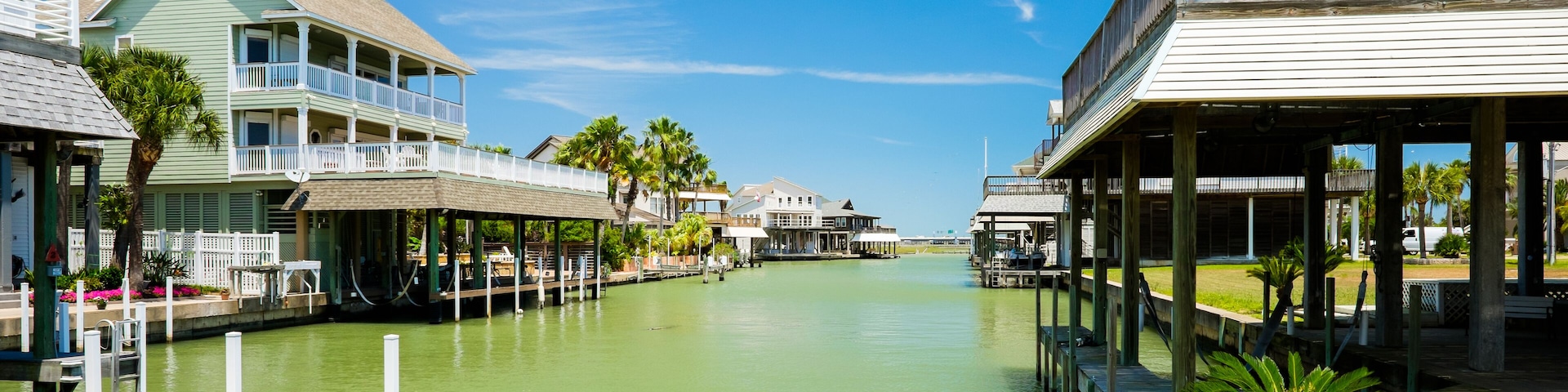 A canal with waterfront houses, palm trees, and a clear blue sky.