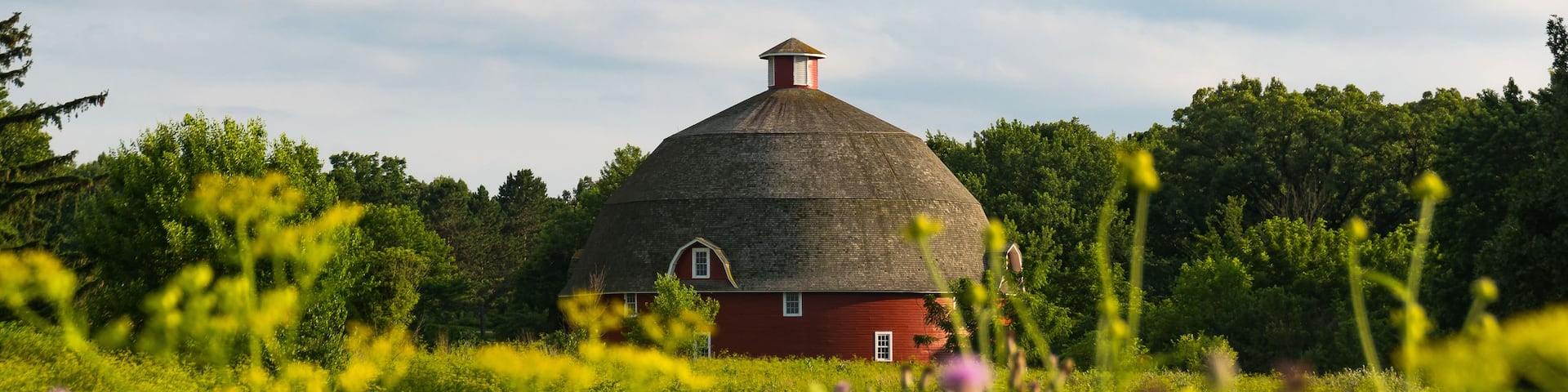 A red barn with a conical roof surrounded by lush greenery and trees.