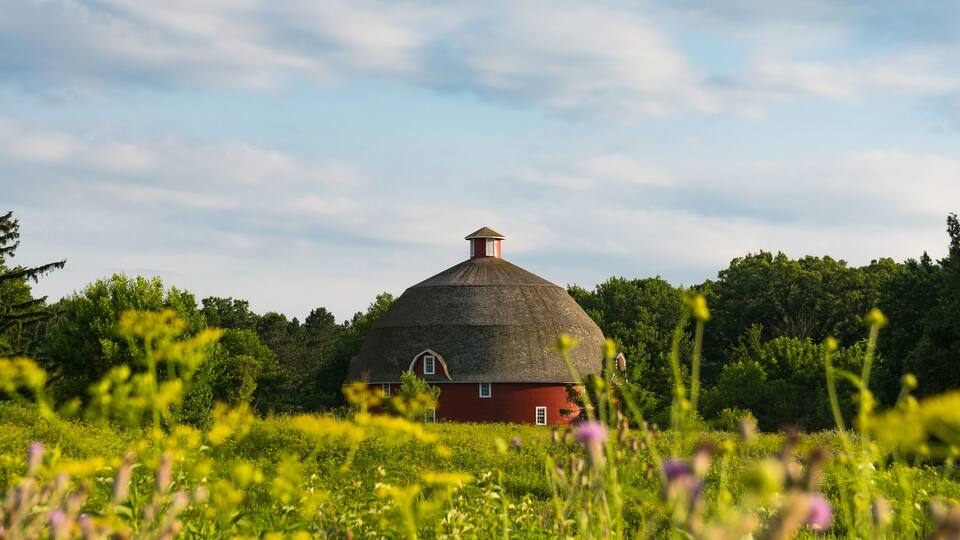 A red barn with a conical roof surrounded by lush greenery and trees.