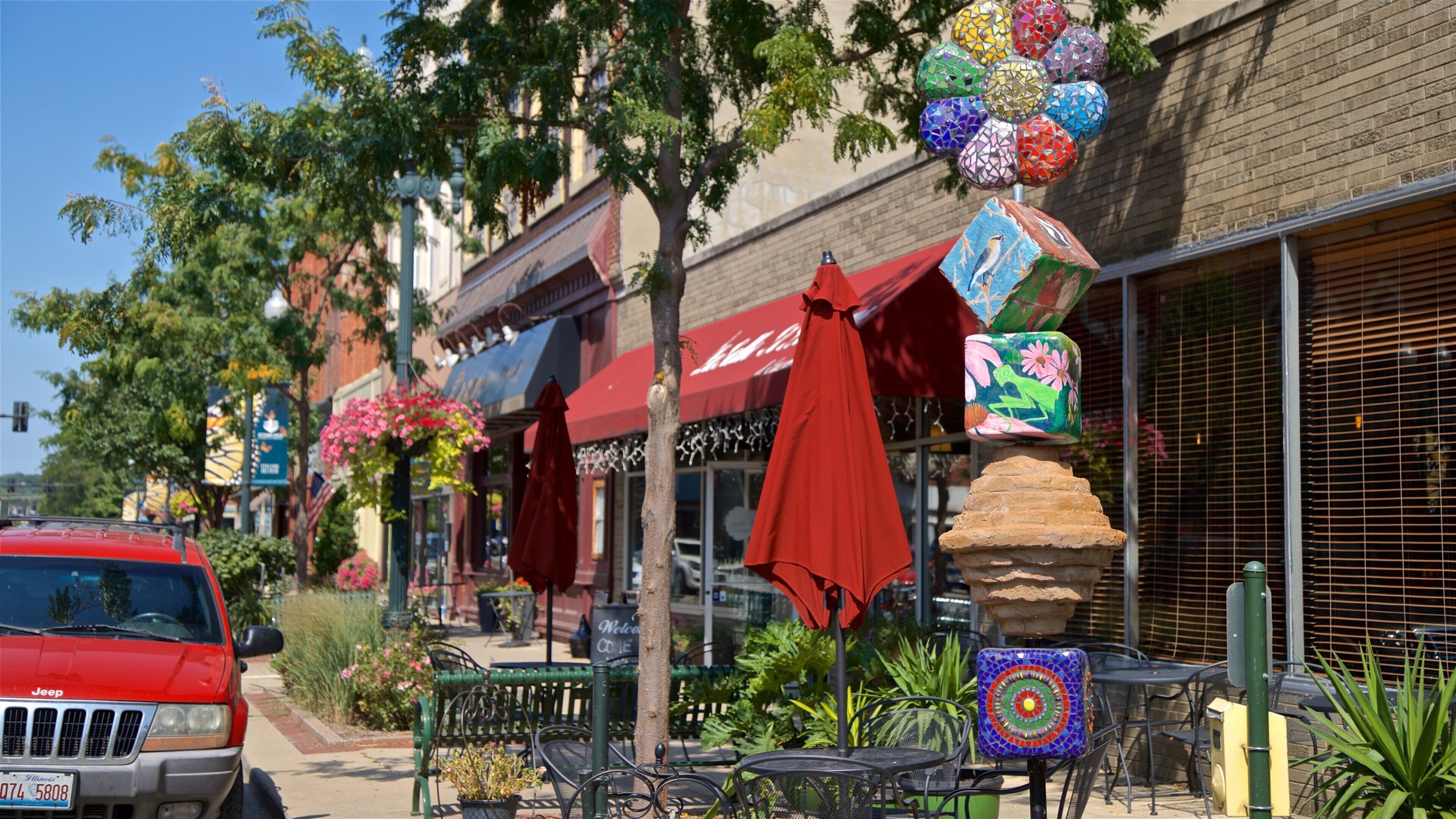 A red Jeep parked on a street with outdoor seating and colorful decorations.