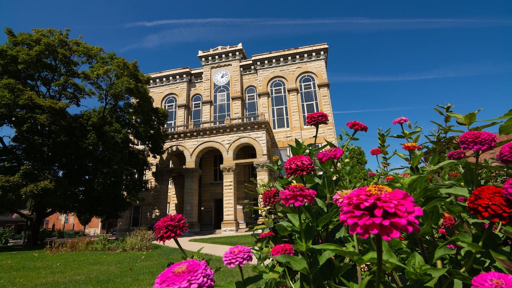 Un bâtiment historique doté d’un clocher, entouré d’un jardin bien entretenu où s’épanouissent de magnifiques fleurs roses.