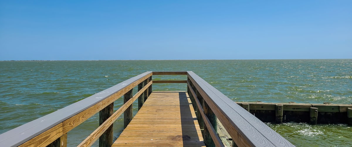 A wooden pier extending into a calm body of water under a clear blue sky.
