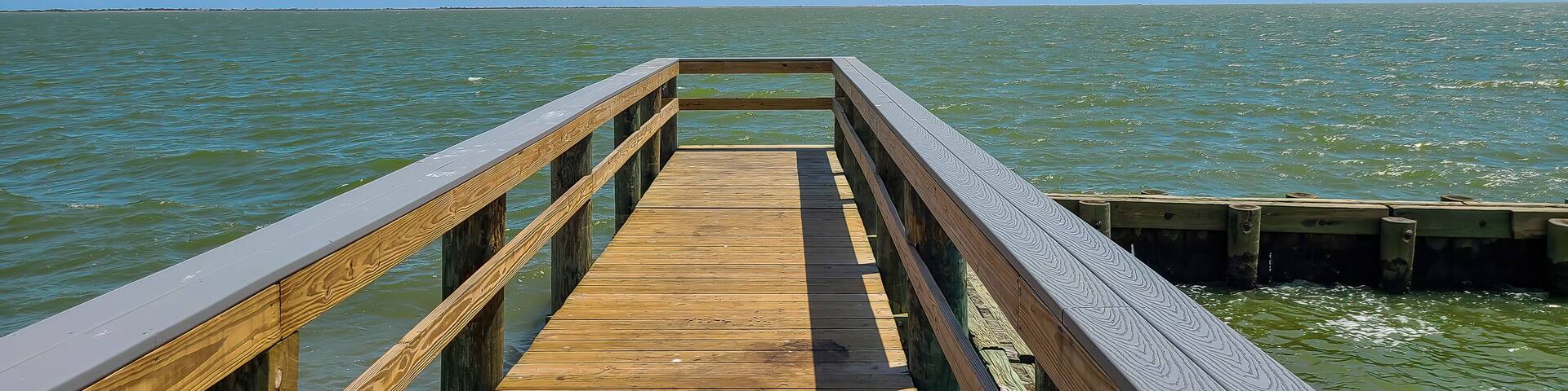 A wooden pier extending into a calm body of water under a clear blue sky.