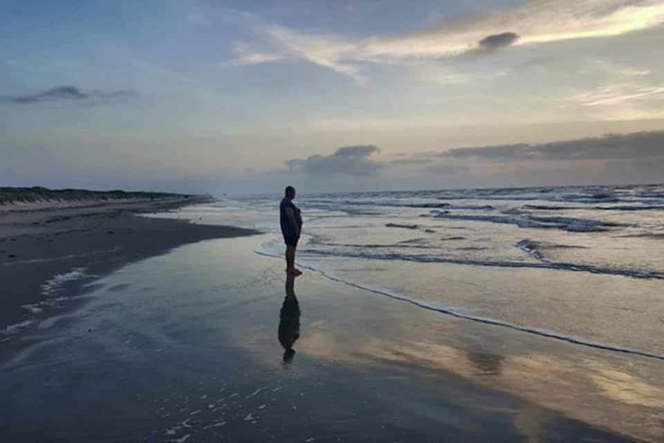 A person standing on a wet beach with waves approaching, under a cloudy sky.